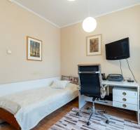 A room in a 4-room apartment with a bed, a desk, and a TV on the wall.