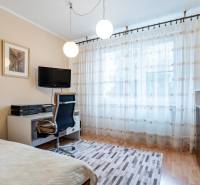 A room in a 4-room apartment with a desk, a television, an armchair, and curtains.
