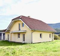 A family house in Buková with a red roof and a grass-covered yard, surrounded by nature.