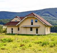 A family house in Buková with a red roof surrounded by green hills in the background.