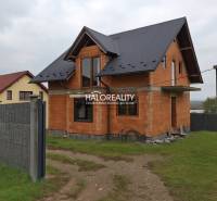 A family house in Sady nad Torysou with an unfinished facade and a dark roof behind a fence.