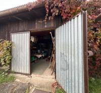 Open metal garage door at a family house in Kalša, surrounded by lush vegetation.
