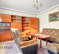 Living room in a family house with armchairs, carpet, bookshelf, and curtains.