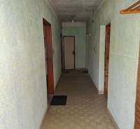 A hallway in a family house with light green walls, tiles, and simple lighting.