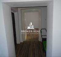 A hallway of a family house with a wooden decor floor and a view into another room.