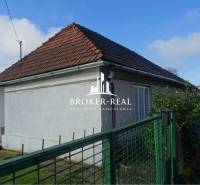 A family house in Rudabánya with a white facade and a sloped roof behind a green fence.