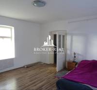 A room with a bed, a window, a floor with a wooden decor, a nightstand, and open doors.