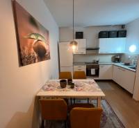 The kitchen of a 2-room apartment with a dining table, yellow chairs, and a wooden-patterned floor.