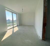 An unfurnished room with a large window, cement floor in a family house.
