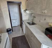 A kitchen in a 3-room apartment with a long countertop and light cabinets.