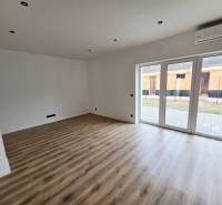 Living room with wood-patterned flooring and large windows in a family house.