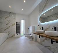A bathroom in a family house with a lighted mirror and marble tiles.