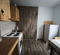 The kitchen in a studio apartment with a wood-patterned floor, wooden cabinets, table.