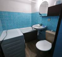 Bathroom with a bathtub, sink, toilet, and washing machine in a studio apartment. Floor with wooden decor.