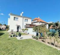 A family house in Partizánske surrounded by a green lawn and a garden under a blue sky.