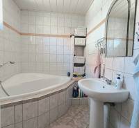 Bathroom in a family house with a corner bathtub, white tiles, and storage baskets.