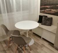 Dining nook with a round table, two chairs, and decorative cushions, floor with wooden decor.