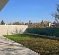 A garden of a family house in Piešťany with a lawn, concrete terrace, and fencing.