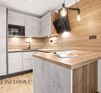 A kitchen with light cabinets, black appliances, and wood-patterned flooring in a two-room apartment.