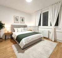 Bright bedroom in a 2-room apartment with wood-patterned flooring, decoration, and a large window.