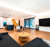 Living room in a family house with a kitchen, stairs, TV, and a wooden decor floor.