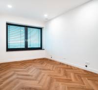 A room in a family house with a wooden decor floor, white walls, and a large window.