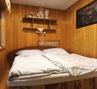 A bedroom in a cottage with a wooden wall and shelves above the bed.