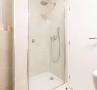 A bathroom with a glass shower enclosure and light tiles in a studio apartment.