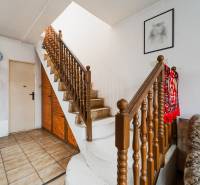 Interior of a family house with a staircase, deep red carpet, and a painting on the wall.