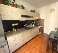 A kitchen in a 3-room apartment with a wooden decor floor, light cabinets, and a dining table.