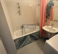 Bathroom with a bathtub, sink, and washing machine in a 3-room apartment, tiled with white tiles.