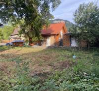 A cottage in Zliechov with a red roof, surrounded by greenery and wood on the property.