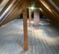 Attic in a cottage with wooden beams and a brick chimney, floor with wooden decor.