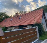 A cottage in Zliechov with a red roof and a wooden fence against the backdrop of mountains.