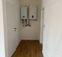 A narrow hallway in a 2-room apartment with a wood-patterned floor and a boiler on the wall.