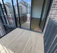 A balcony with a wooden decor floor in a 2-room apartment, overlooking buildings.