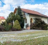 A villa on Andreja Sládkoviča Street in Žarnovica, surrounded by greenery, with a church in the background.