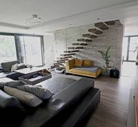 Living room with a comfortable sofa, open staircase, and large windows, designed on Jánošíkova Street.
