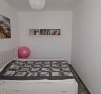 A bedroom with a bed, a painting, books, and a wooden decor floor in a 3-room apartment.