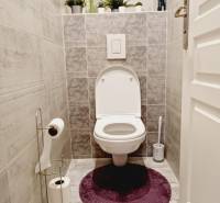 A toilet in a 3-room apartment with decorations, white sanitary ware, and gray tiles.