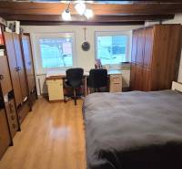A room in a family house with a wooden decor floor, a bed, and an office corner.