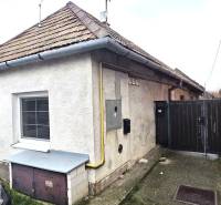 Family house in Dolné Orešany, gray plaster, two windows, sloped roof, adjacent cars.