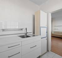 A kitchen in a studio apartment with white kitchen cabinets and a view into the living room.