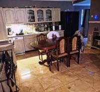A kitchen in a family house with ceramic tiles, wooden cabinets, and a dining table.
