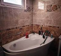 Bathroom in a family house with a bathtub and a tiled wall.