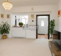 A living room in a family house with white walls, flowers, and a television on a table.