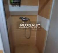 A shower corner in a one-room apartment with orange tiles and wall storage space.