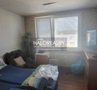 A room in a one-bedroom apartment with a bed, chair, television, and a large window.