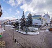 A street in Poprad with commercial buildings, a winter scene, and snow-covered trees.
