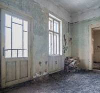 The interior of the building with damaged walls, doors, and windows, bricks on the floor.